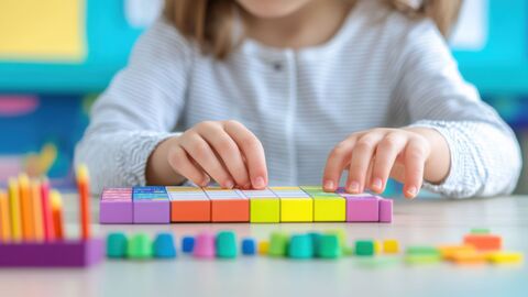 Kind ordnet bunte Rechenwürfel am Tisch an Ein Kind sitzt am Tisch und ordnet mit beiden Händen bunte Recenwürfel an.