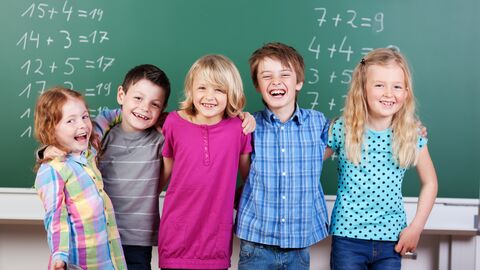 Mathematik-Unterricht Junge Schülerinnen und Schüler stehen vor einer mit Mathematik-Aufgaben beschriebenen Tafel, haben die Arme umeinander gelegt und lächeln